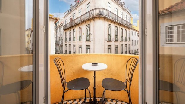 En balkon med et bord og to stole, med udsigt over en bygning med flere vinduer og balkoner.