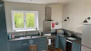 Een moderne keuken met blauwgroene kastjes, een roestvrijstalen afzuigkap, een inbouwoven, een spoelbak en een raam met uitzicht op groen.
