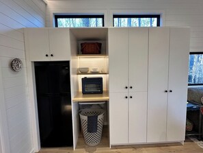 A compact kitchen with a built-in refrigerator, a microwave, and a small shelf with dishes.