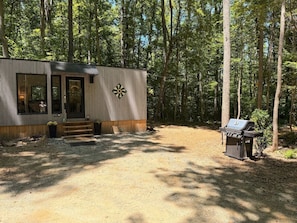 A cabin with a front door, a small porch, and a grill area.
