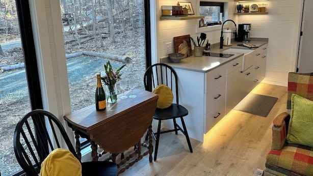 A modern kitchen with a large window, wooden dining table, and chairs. - Riverside Studio | Trails, Views, Firepit, Hammock (Elon)