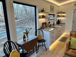 A modern kitchen with a large window, wooden dining table, and chairs. - Riverside Studio | Trails, Views, Firepit, Hammock (Elon)