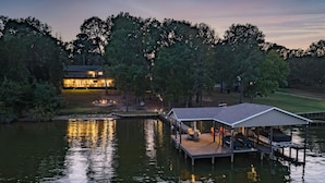 Una propiedad junto al lago con un muelle, una zona de estar cubierta y una casa al fondo.