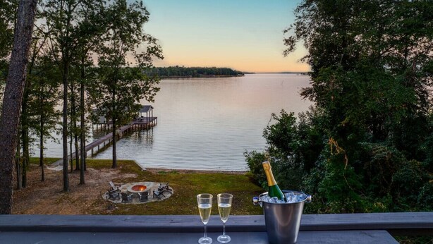 Vista de un lago con un muelle, una fogata y una botella de champán sobre una mesa.