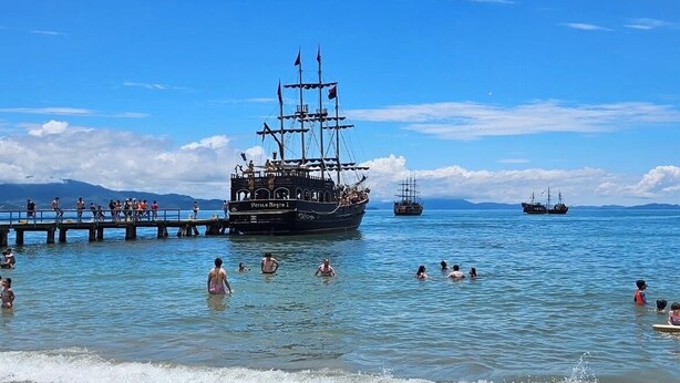 A beach with a ship named 'Perla Negra 1' anchored near the shore, people swimming in the water, and a clear blue sky. - Viva Canasvieiras Apartment 50m from the beach (Florianópolis)