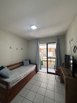A bedroom with a bed, a desk with a TV, a balcony with a view, and a ceiling light. - Viva Canasvieiras Apartment 50m from the beach (Florianópolis)