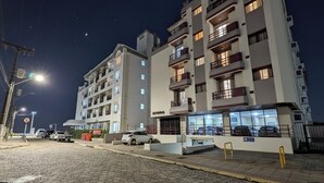 A multi-story hotel with a modern design, featuring balconies on each floor and a parking area in front. - Viva Canasvieiras Apartment 50m from the beach (Florianópolis)
