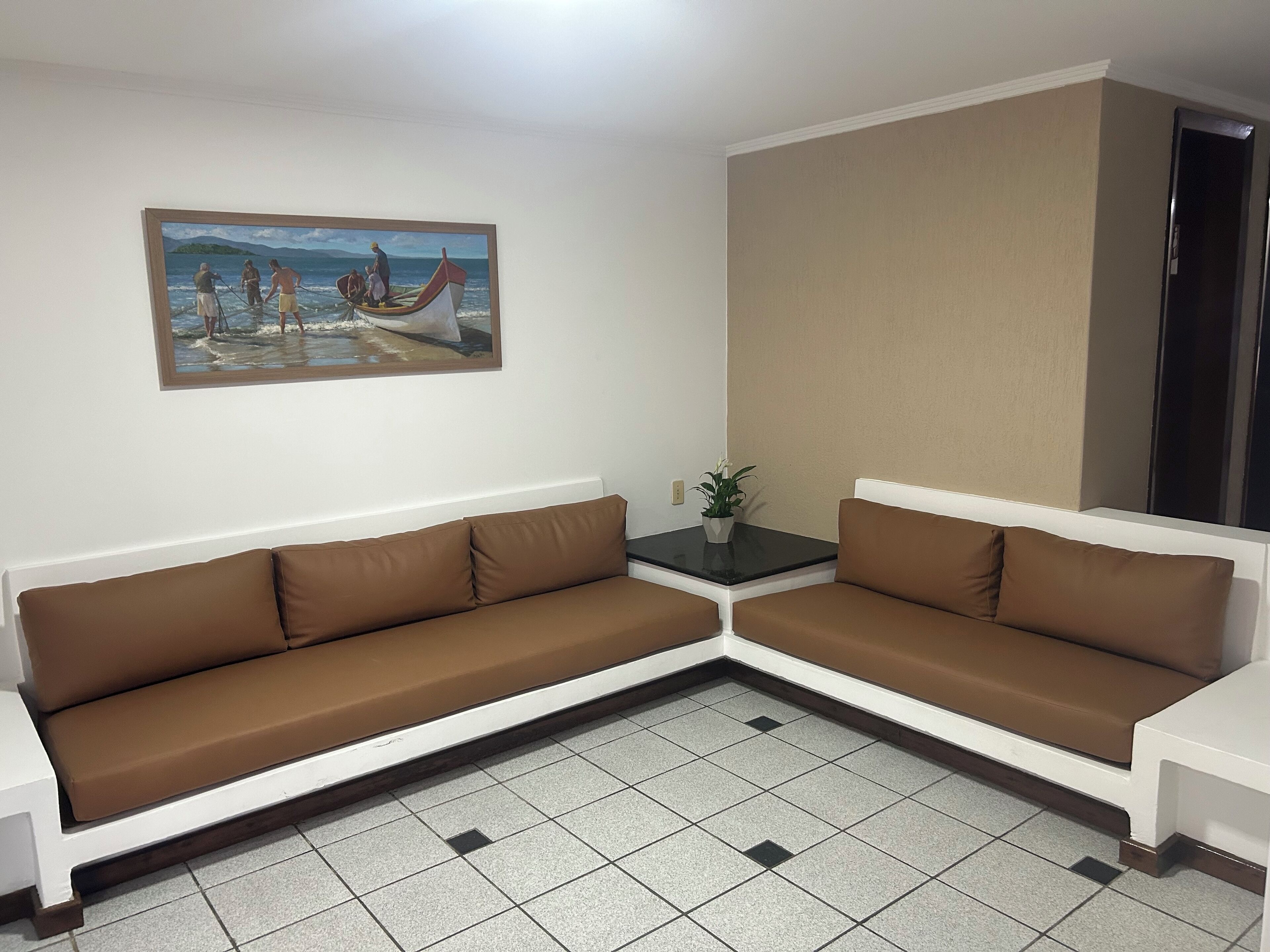 Un salon avec un canapé marron, une petite table sur laquelle est posée une plante, et un tableau représentant une scène de plage.