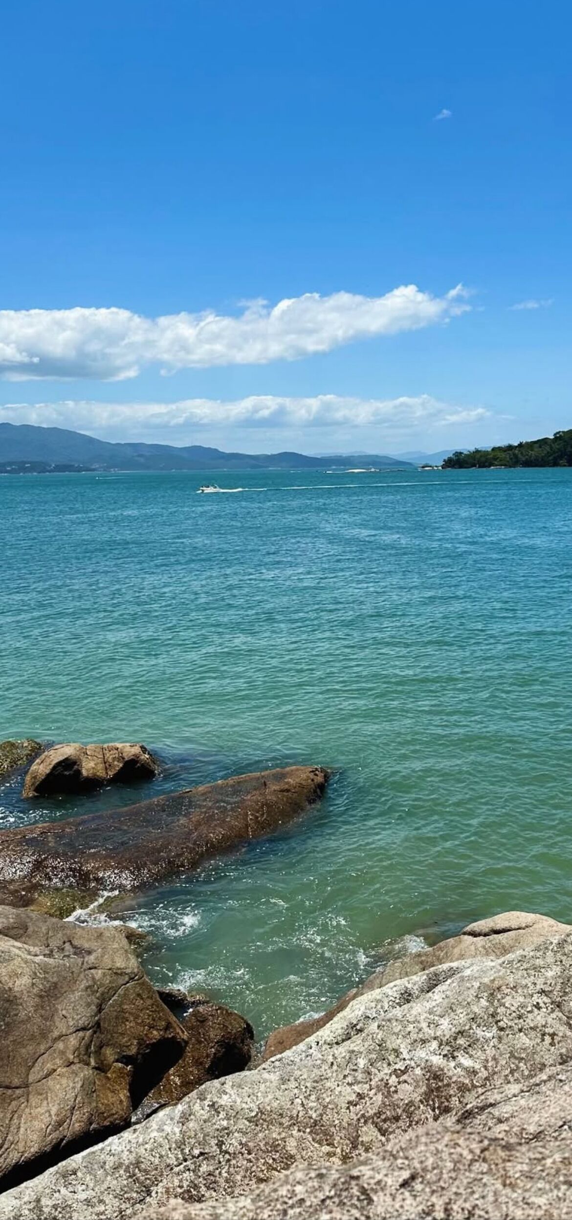 Una vista despejada de un lago con aguas tranquilas, rodeado de grandes rocas y montañas distantes bajo un cielo azul.