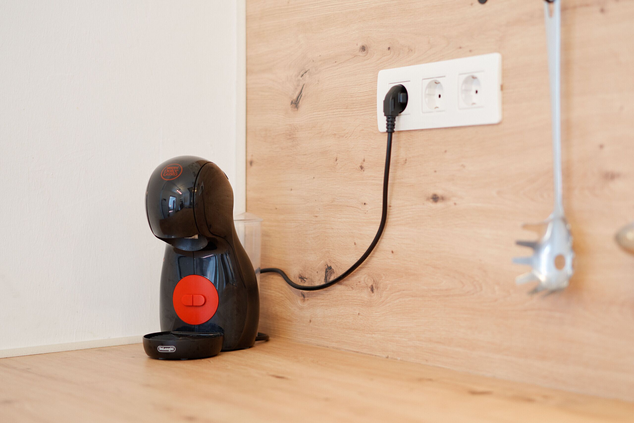 Una máquina de café con un botón rojo, conectada a un enchufe de pared.