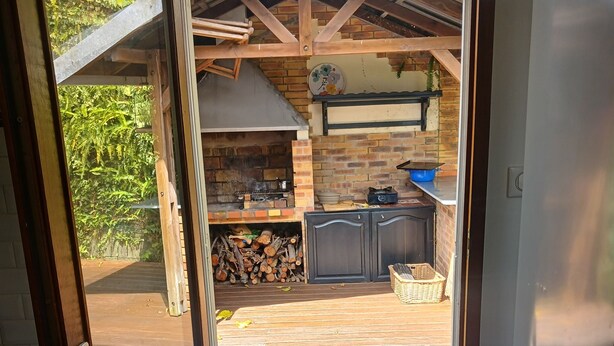 Eine offene Tür zu einem Patio mit Kamin aus Ziegelsteinen, einer Holzterrasse und einer Küche mit blauer Arbeitsplatte.