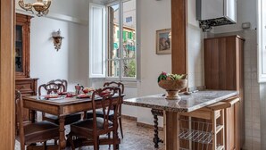 A dining area with a wooden table and chairs, a marble countertop, and a view through a window. - Beautiful and spacious modern apartment in Florence, located in the quiet and well-connected Campo di Marte area. Situated on the first floor, the apartment can accommodate up to 7 guests with 2 double beds and 3 single bed, arranged across 4 bedrooms. I (Firenze)