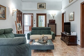 A living room with two green sofas, a coffee table with a bottle and glasses, and a TV stand with a television. - Beautiful and spacious modern apartment in Florence, located in the quiet and well-connected Campo di Marte area. Situated on the first floor, the apartment can accommodate up to 7 guests with 2 double beds and 3 single bed, arranged across 4 bedrooms. I (Firenze)