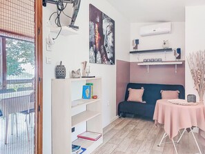 A room with a blue sofa, a pink table, and a bookshelf with books and decorative items. - Chalet Terra Tramandera by Interhome (Calcatoggio)