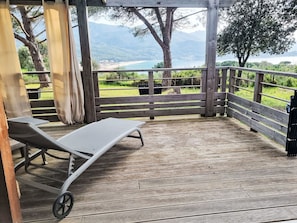 A wooden deck with a lounge chair, wooden railing, and a view of a beach and mountains. - Chalet Terra Tramandera by Interhome (Calcatoggio)