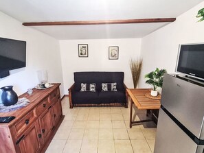 Ein kompakter Wohnraum mit Küchenzeile, einer Couch mit gemusterten Kissen, einem Holztisch und einem Fernseher.