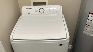 Samsungin etuaukollinen pyykinpesukone pyykinhuoneessa, jossa on harmaa lämminvesivaraaja ja ovi vasemmalla puolella.