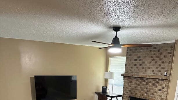 Ein Wohnzimmer mit Fernseher, Kamin, Ledersofa und einem gemusterten Teppich.