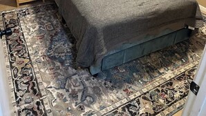 Ein Schlafzimmer mit einem Bett, zwei Nachttischen, einem Fenster mit Jalousien und einem gemusterten Teppich.