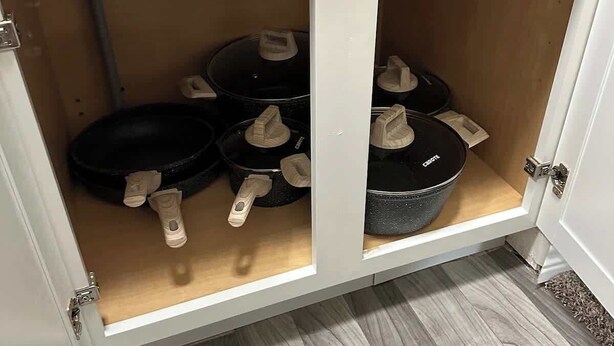 Un mueble de cocina con dos estantes abiertos que contienen sartenes negras y asas blancas.