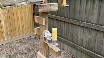 Eine Holzkonstruktion mit einem Vogelhaus, einem hängenden Gegenstand und einem Kerzenständer.