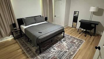 A modern bedroom with a bed, a desk, a chair, a standing lamp, a ceiling fan, and a large rug.