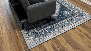 Una sala de estar con un sofá seccional gris, un tapete estampado, un televisor de pantalla plana montado en la pared y piso de madera.