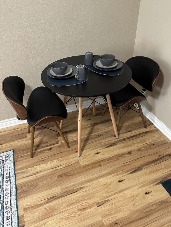A round dining table with four black chairs, each with wooden legs. The table is set with plates, bowls, and a cup.