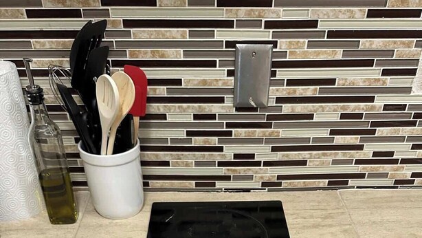 Una cocina con tope de inducción negro, salpicadero de azulejos y encimera con diversos utensilios y una botella de aceite de oliva.