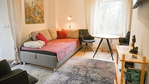 Une pièce confortable avec un lit, une chaise, une petite table et une fenêtre donnant sur des arbres.