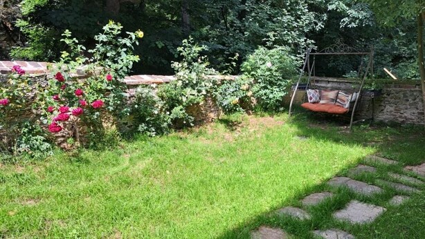 Un jardin avec un chemin de pierre, une balançoire et un mur en pierre.