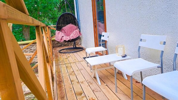 Une terrasse en bois avec des chaises blanches et un fauteuil suspendu doté d’un coussin rose.