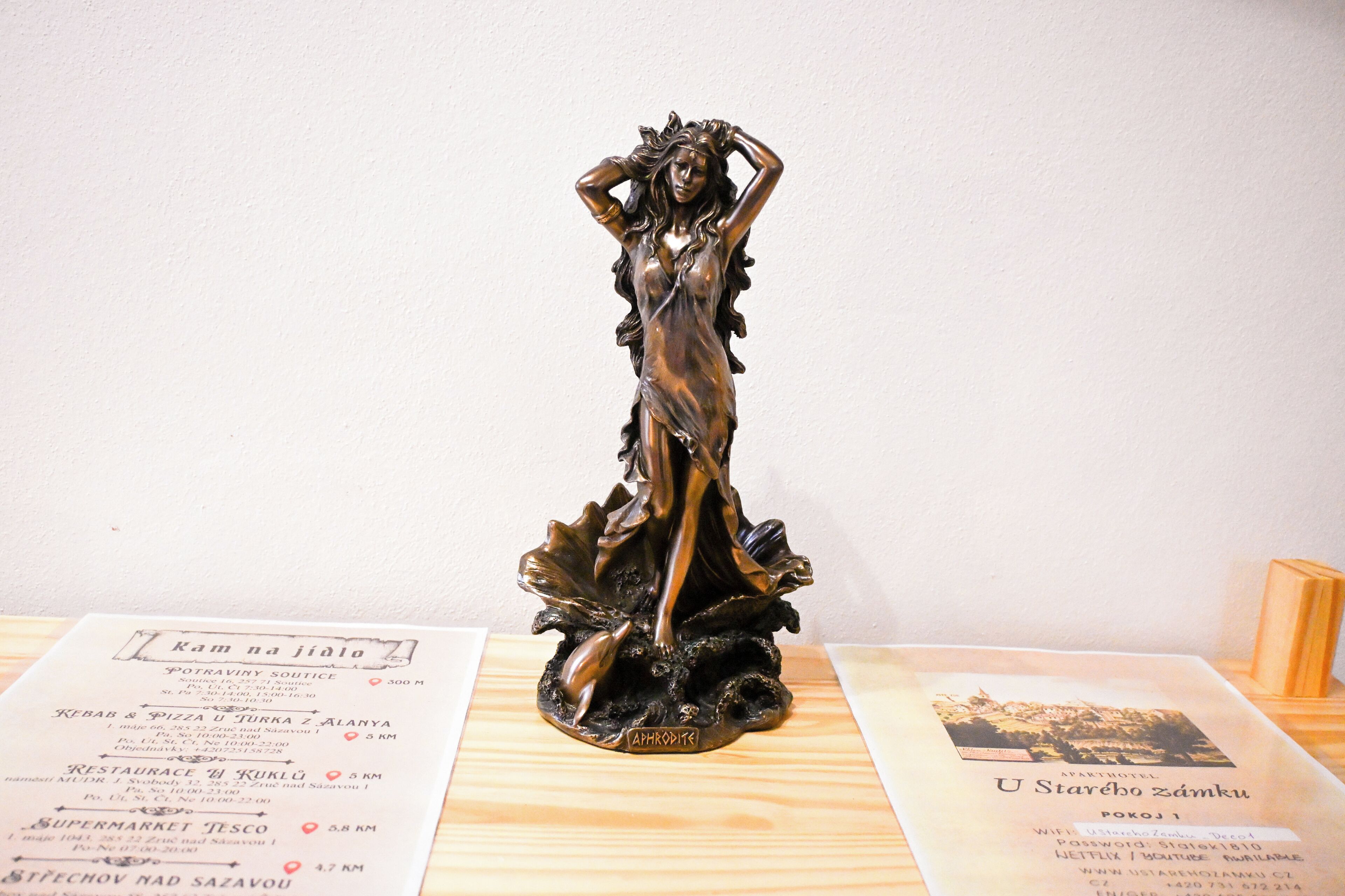 Estátua de bronze de uma mulher em pedestal, colocada sobre uma superfície de madeira com um menu na frente.