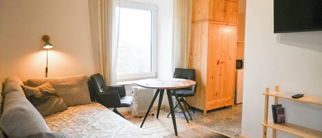 A cozy room with a bed, a desk, a chair, a small table, and a TV mounted on the wall.