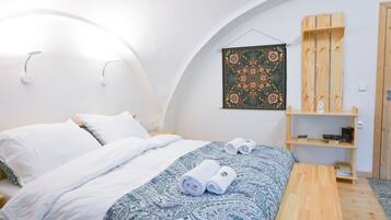 A bedroom with a bed, pillows, a bedside table, a wall-mounted artwork, and a wooden shelf.