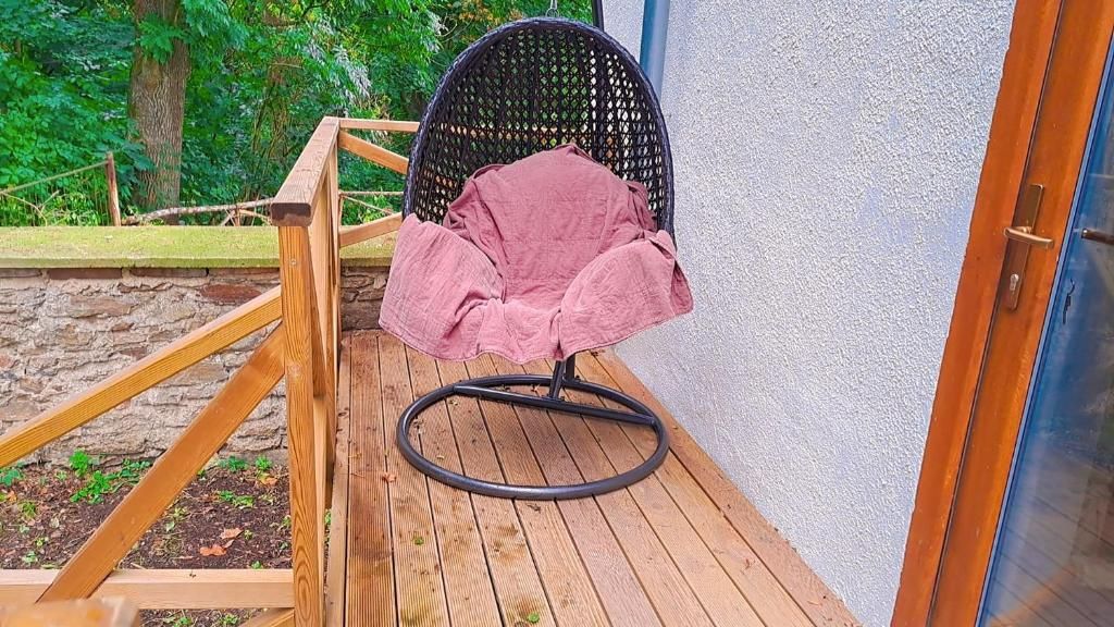 Una terraza de madera con una silla de ratán negro y un cojín rosa.