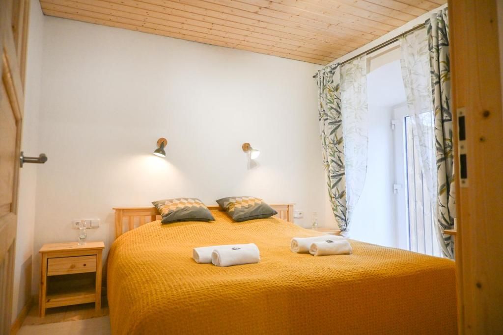 A bedroom with a wooden ceiling, a bed with a yellow blanket, two bedside lamps, and a window with curtains.