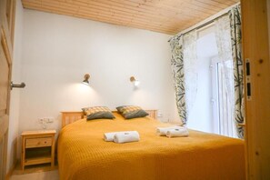 Une chambre à coucher avec un plafond en bois, un lit recouvert d’une couverture jaune, deux lampes de chevet et une fenêtre avec des rideaux.