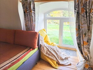 Une pièce avec un canapé, une fenêtre avec des rideaux et une vue sur un paysage verdoyant.