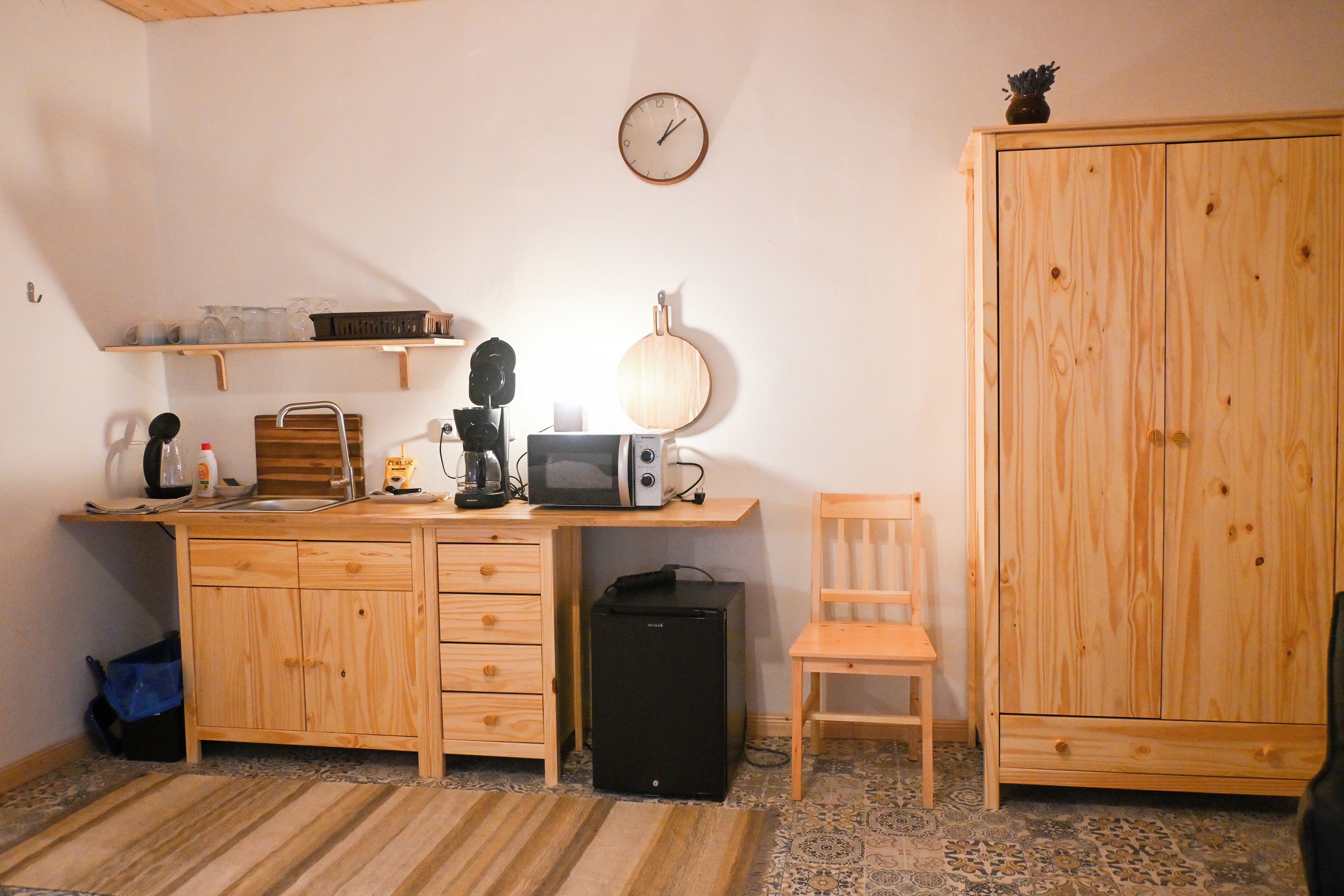 Habitació compacta amb escriptori de fusta, una cadira, un armari i un rellotge de paret.