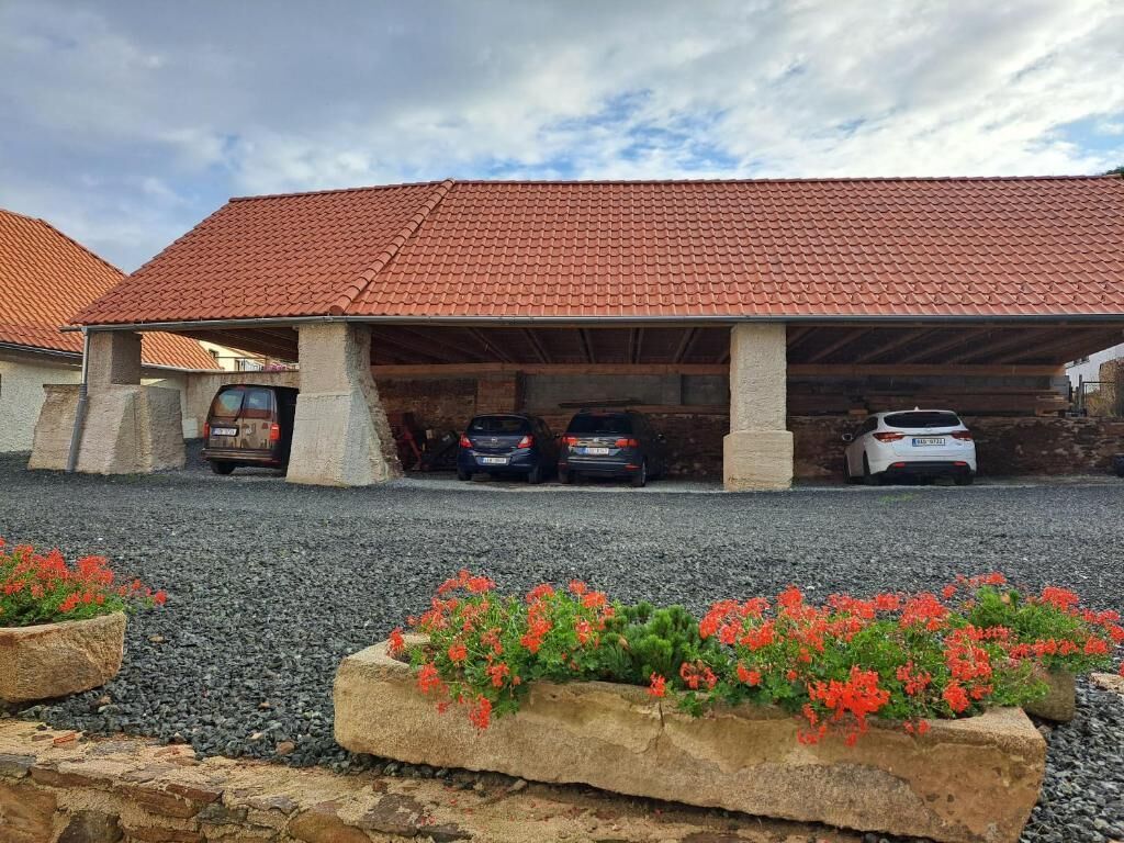A building with a red-tiled roof, covered parking area, and three cars parked under the structure.