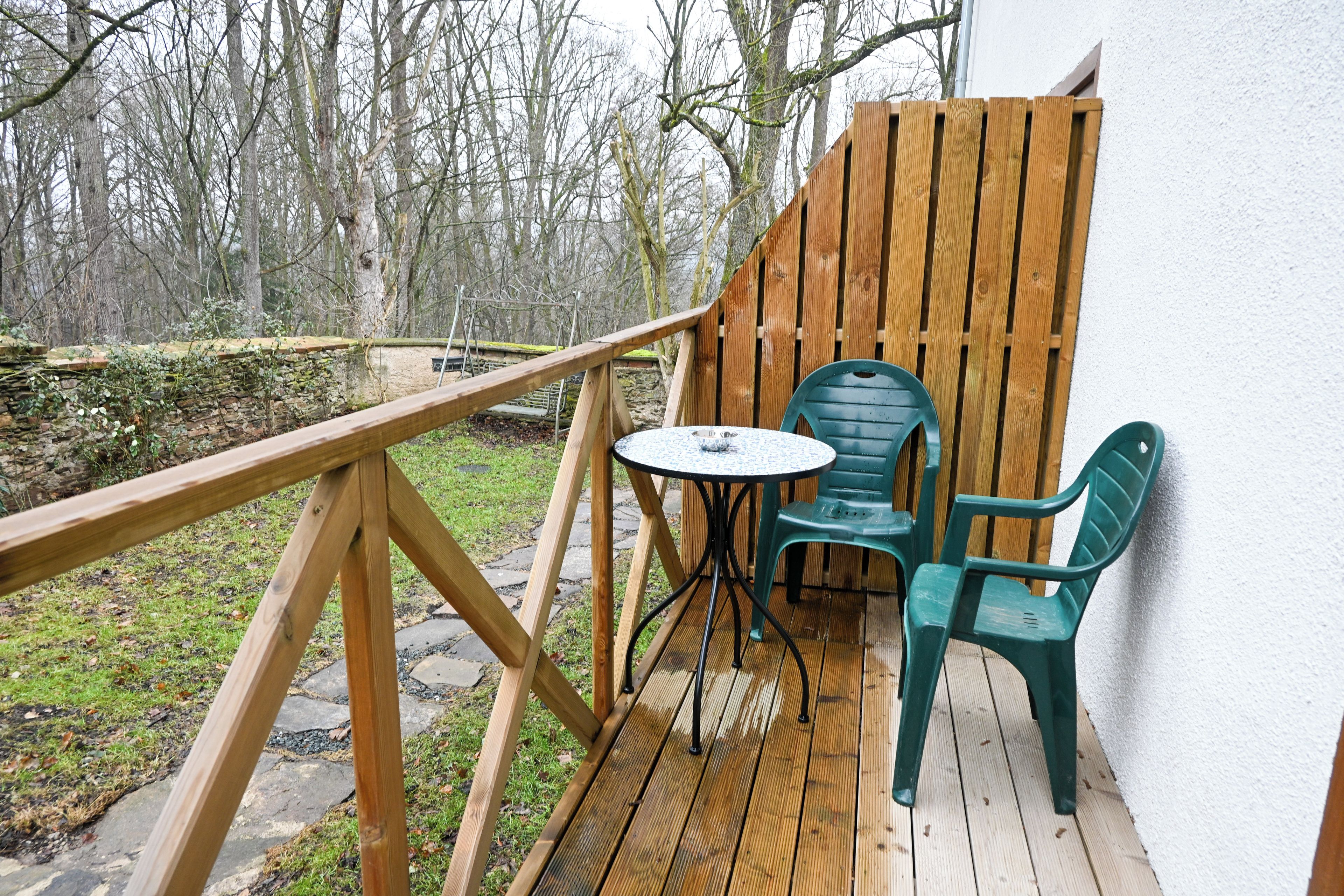 A wooden deck with a table and chairs, a stone wall, and a view of trees.