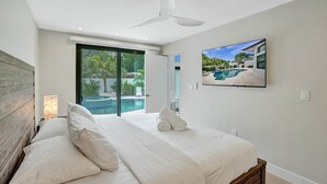 A bedroom with a large bed, a ceiling fan, a TV, and a view of a swimming pool. - Deerfield Luxury Stay: Heated Pool, Hot Tub & Golf (Deerfield Beach)