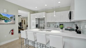 A modern kitchen with white cabinetry, a large island with bar stools, stainless steel appliances, and a view of a swimming pool. - Deerfield Luxury Stay: Heated Pool, Hot Tub & Golf (Deerfield Beach)