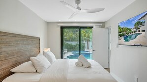 Un dormitori amb un llit gran, un ventilador de sostre i vista a una piscina.