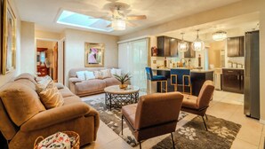 A spacious living area with a sofa, armchairs, and a coffee table. There is a kitchen area with modern appliances and bar stools. - Ocala - WEC. (Ocala)