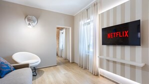 A modern living room with a flat-screen TV, a white armchair, and a sofa. - Hostdomus - The Court (Alba)