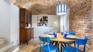 A dining area with a brick wall, wooden cabinet, and blue chairs. - Hostdomus - The Court (Alba)