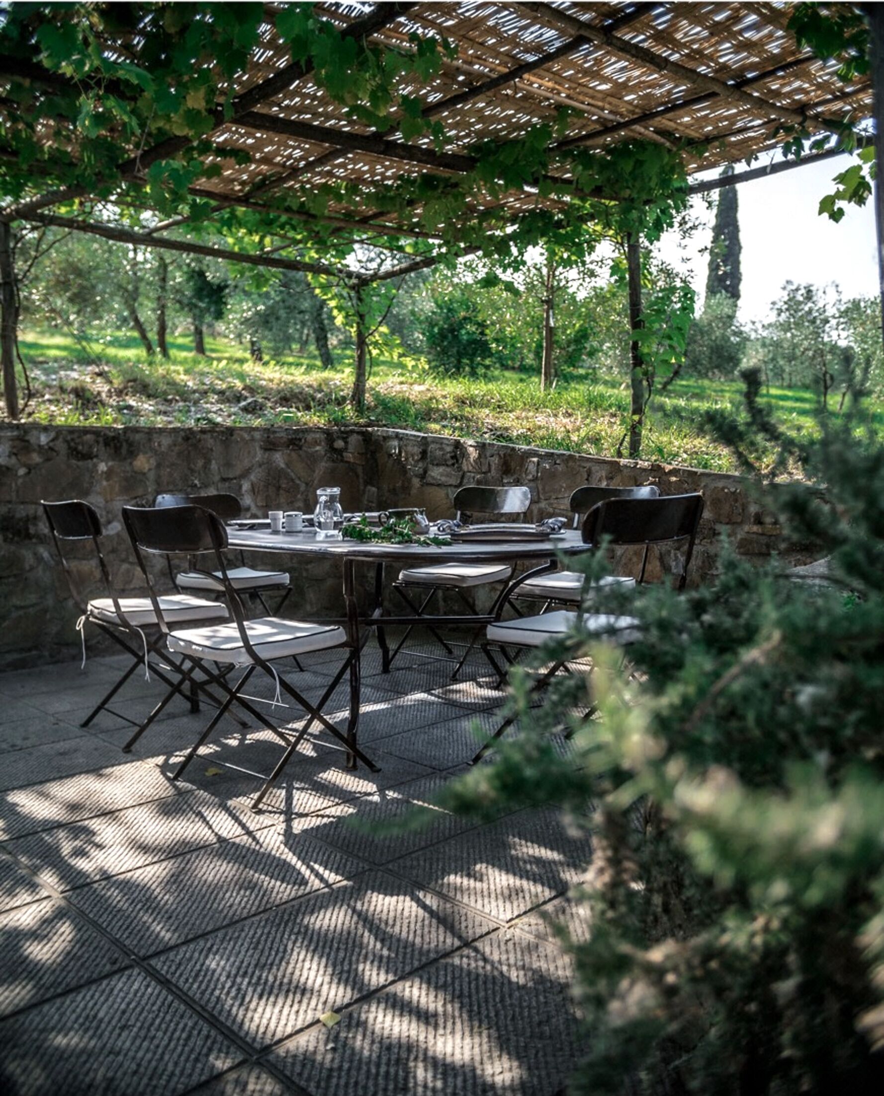 Un área de comedor al aire libre con una pérgola, paredes de piedra y vistas a un viñedo.