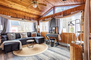 Un acogedor interior de cabaña con techo de madera, un conjunto de sofás, un escritorio y un gran ventanal.